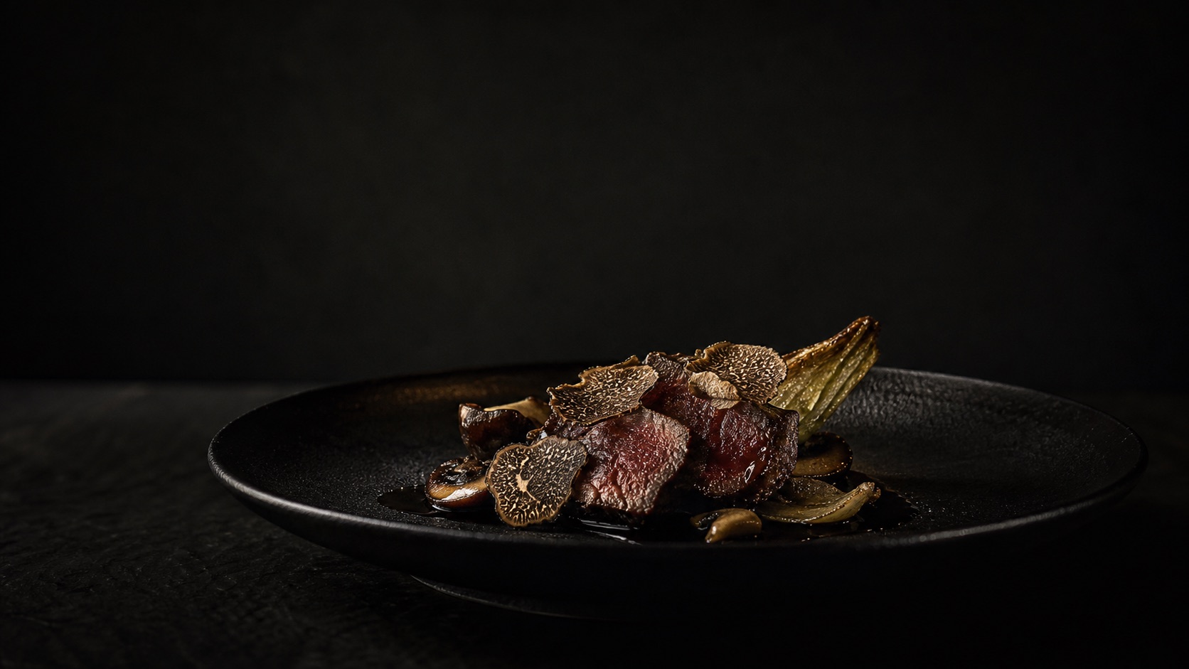 黒トリュフと肉料理を黒い皿に盛ったコース料理